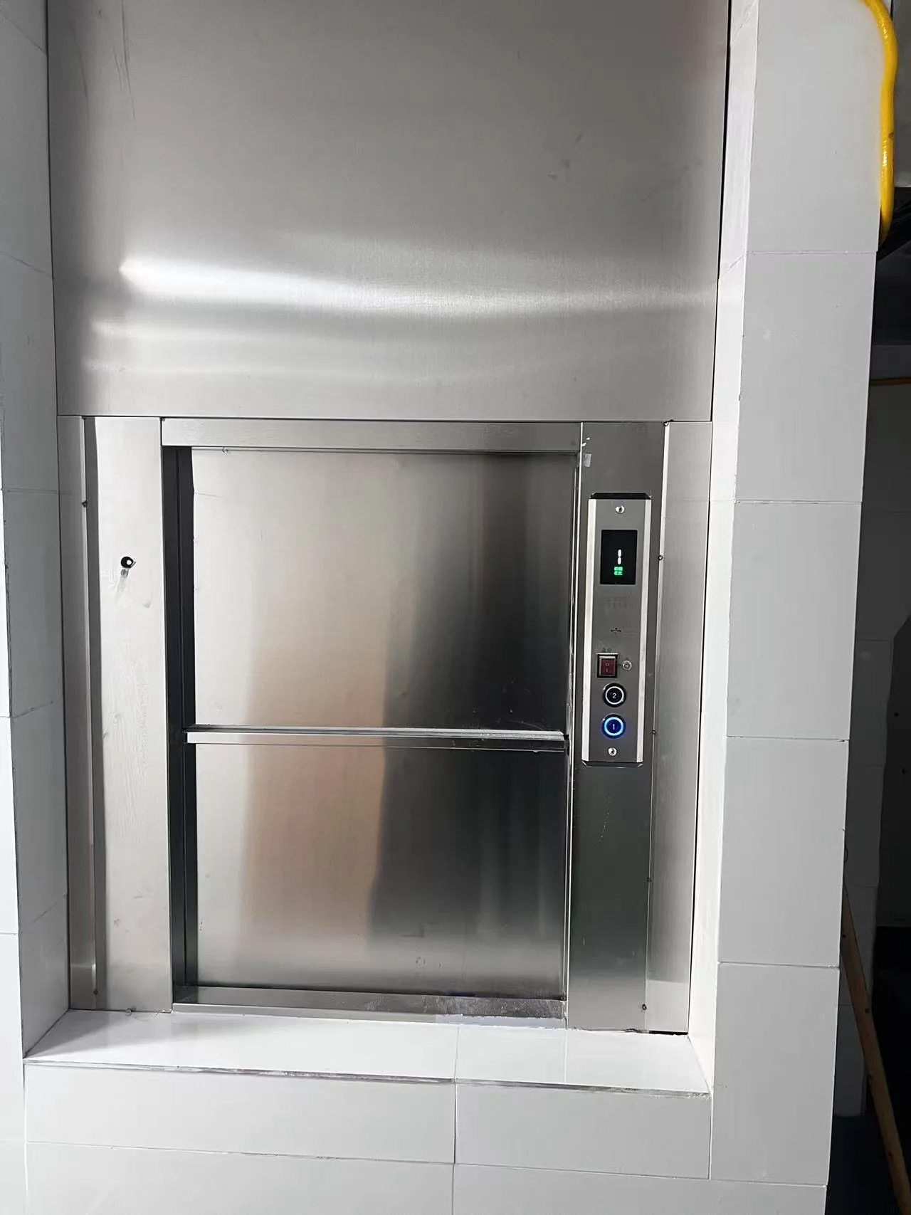 GOELEV dumbwaiter installed on site — stainless steel car with side-mounted call station in tiled wall